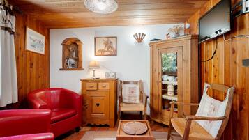 A cozy room with wooden walls, a red leather sofa, a wooden cabinet, a wicker chair, and a television mounted on the wall.