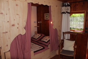 A wooden cabin room with a bed, a chair, and a window with a view. - Gîte Les Croës – Chalet Les Abeillos (Bonneval-sur-Arc)