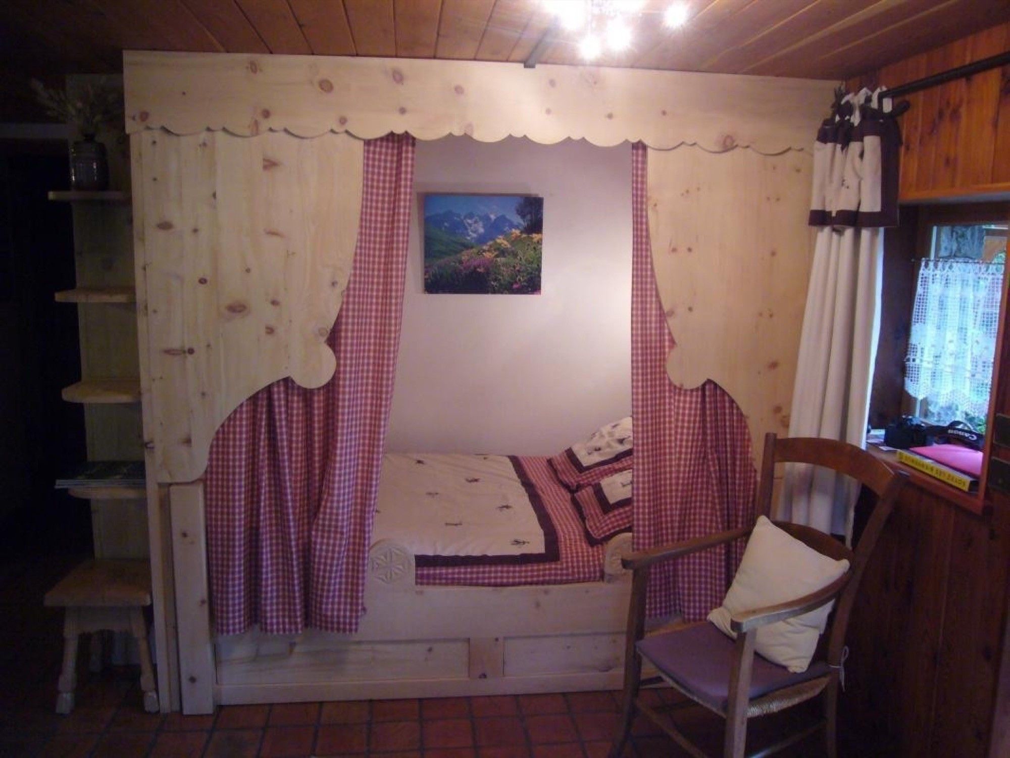 Een knus ingerichte kamer met een bed, een stoel, een schilderij en een raam met gordijnen.