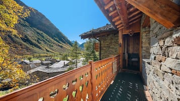 Un balcon en bois orné de motifs en forme de cœur, donnant sur une vallée parsemée de bâtiments traditionnels, avec une chaîne de montagnes en arrière-plan.