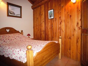 Una cama con estructura de madera y colcha floral en una habitación con paredes de madera y suelo de baldosas.
