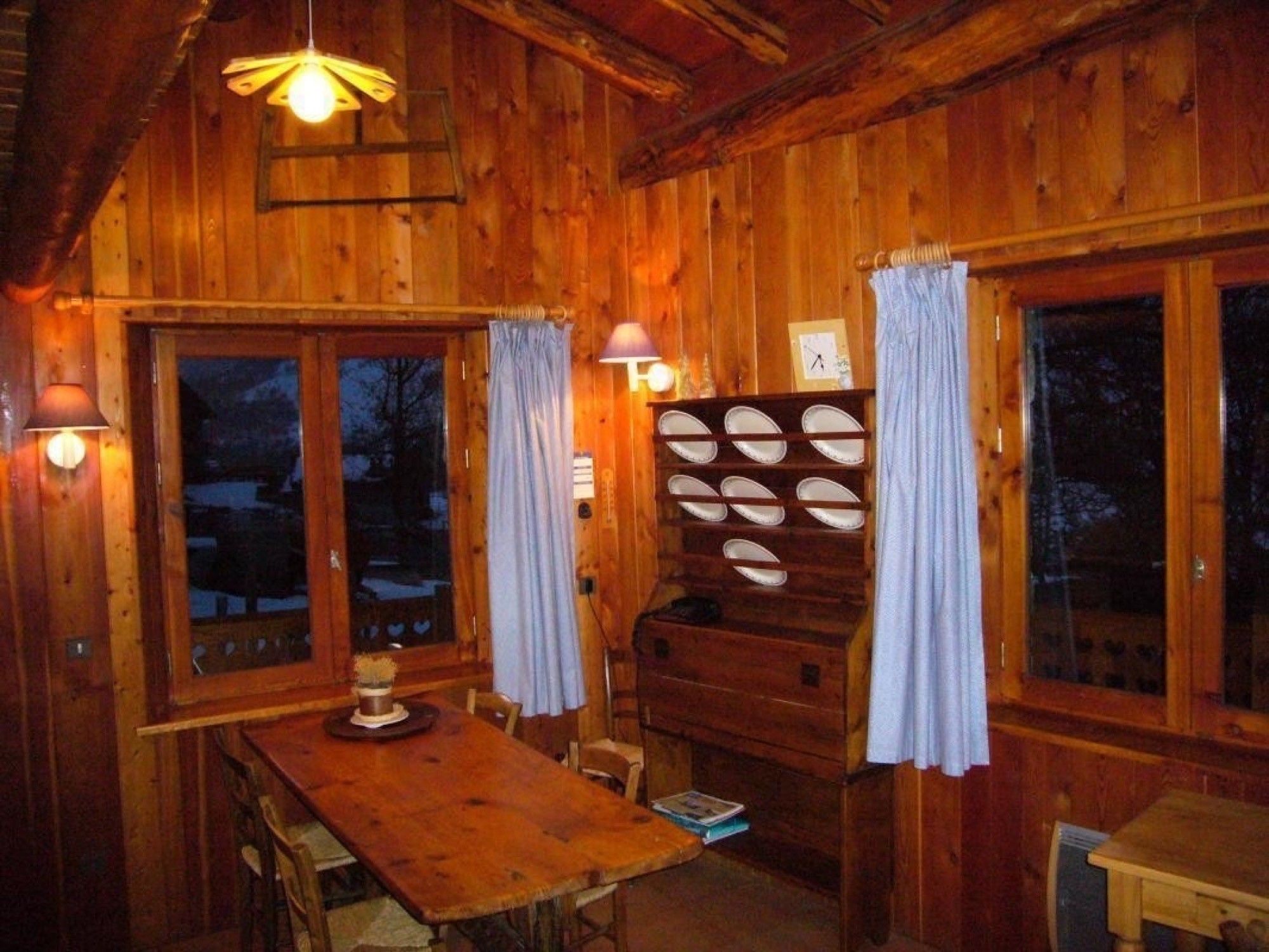 Ein Holzhütten-Interieur mit Esstisch, Stühlen, einer Lampe und einem Schrank mit mehreren Regalen.