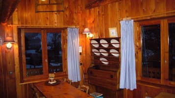 Ein Holzhütten-Interieur mit Esstisch, Stühlen, einer Lampe und einem Schrank mit mehreren Regalen.