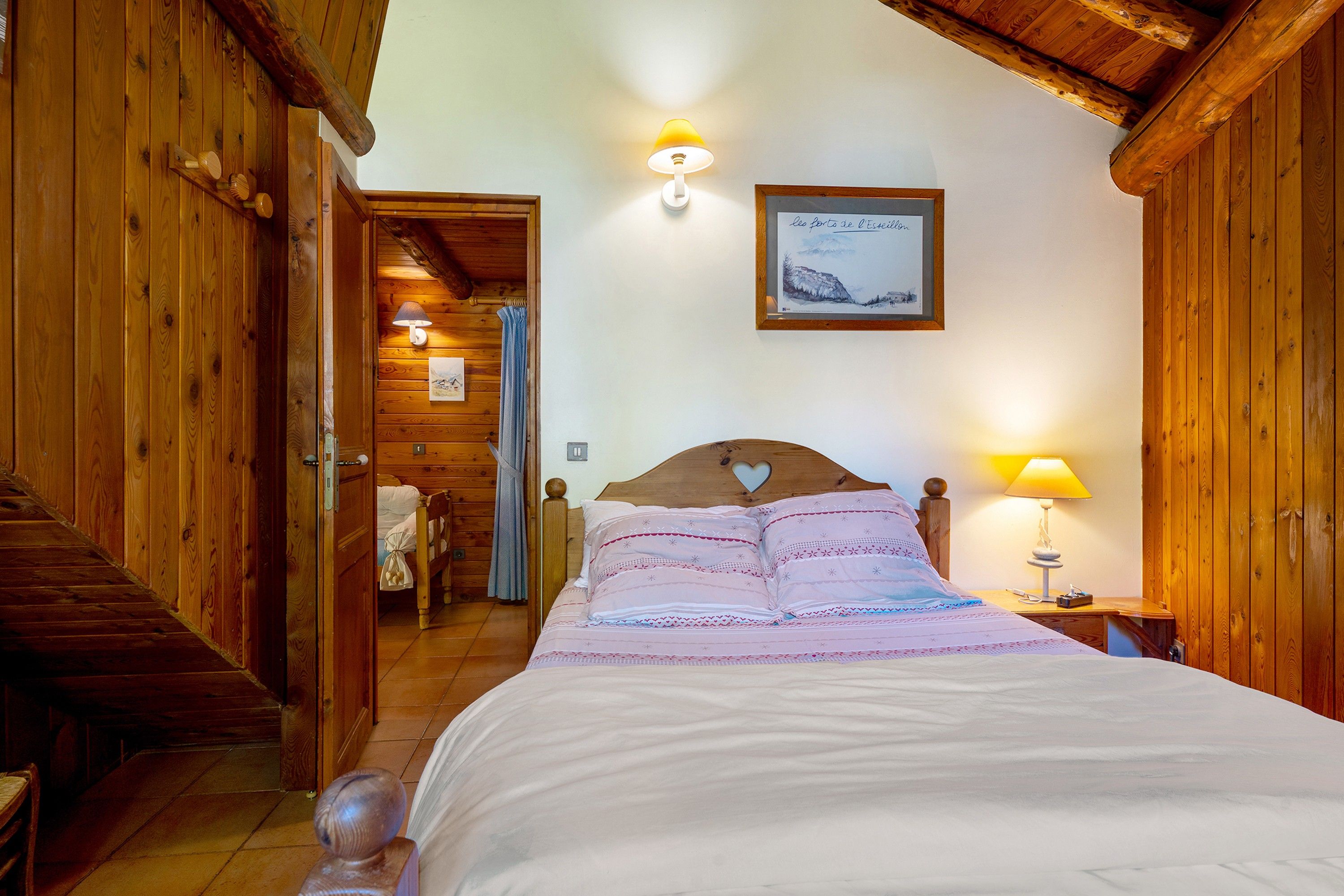 A wooden room with a bed, a nightstand, a lamp, and a framed picture on the wall.