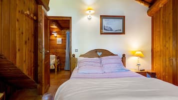 A wooden room with a bed, a nightstand, a lamp, and a framed picture on the wall.