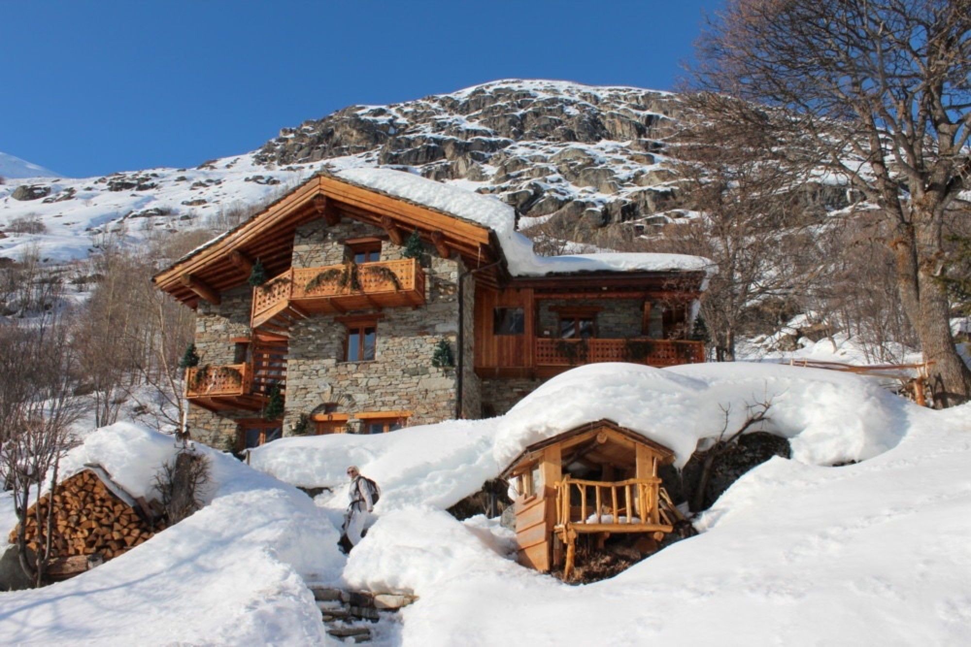 Una cabaña de piedra con balcones de madera, rodeada de nieve y un paisaje montañoso.