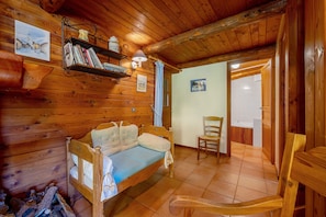 A cozy wooden cabin room with a bed, a chair, a shelf with books, and a painting on the wall.