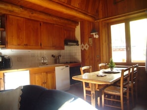 Interior de una cabaña de madera con cocina, mesa de comedor y sillas.