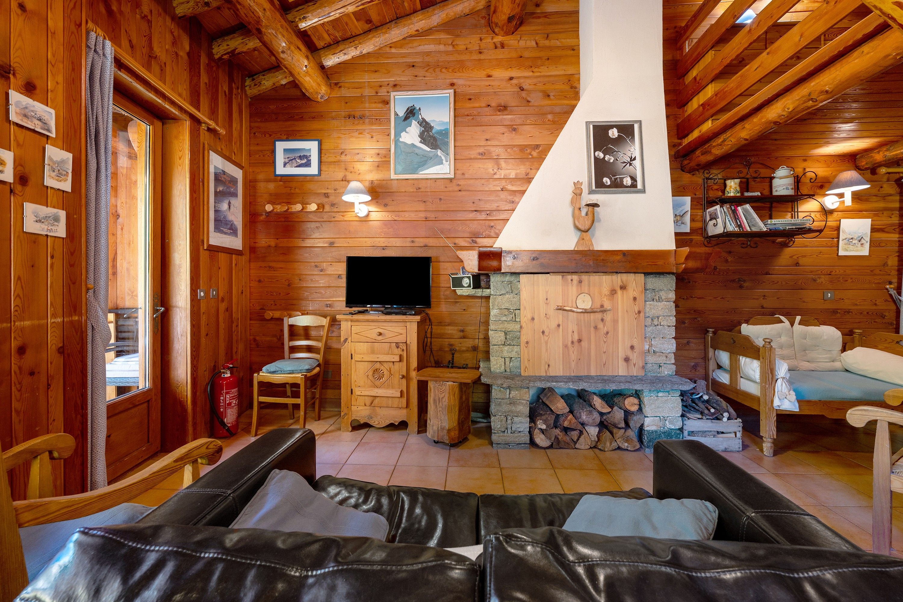 A cozy cabin interior with a fireplace, wooden walls, a television, and a bed.