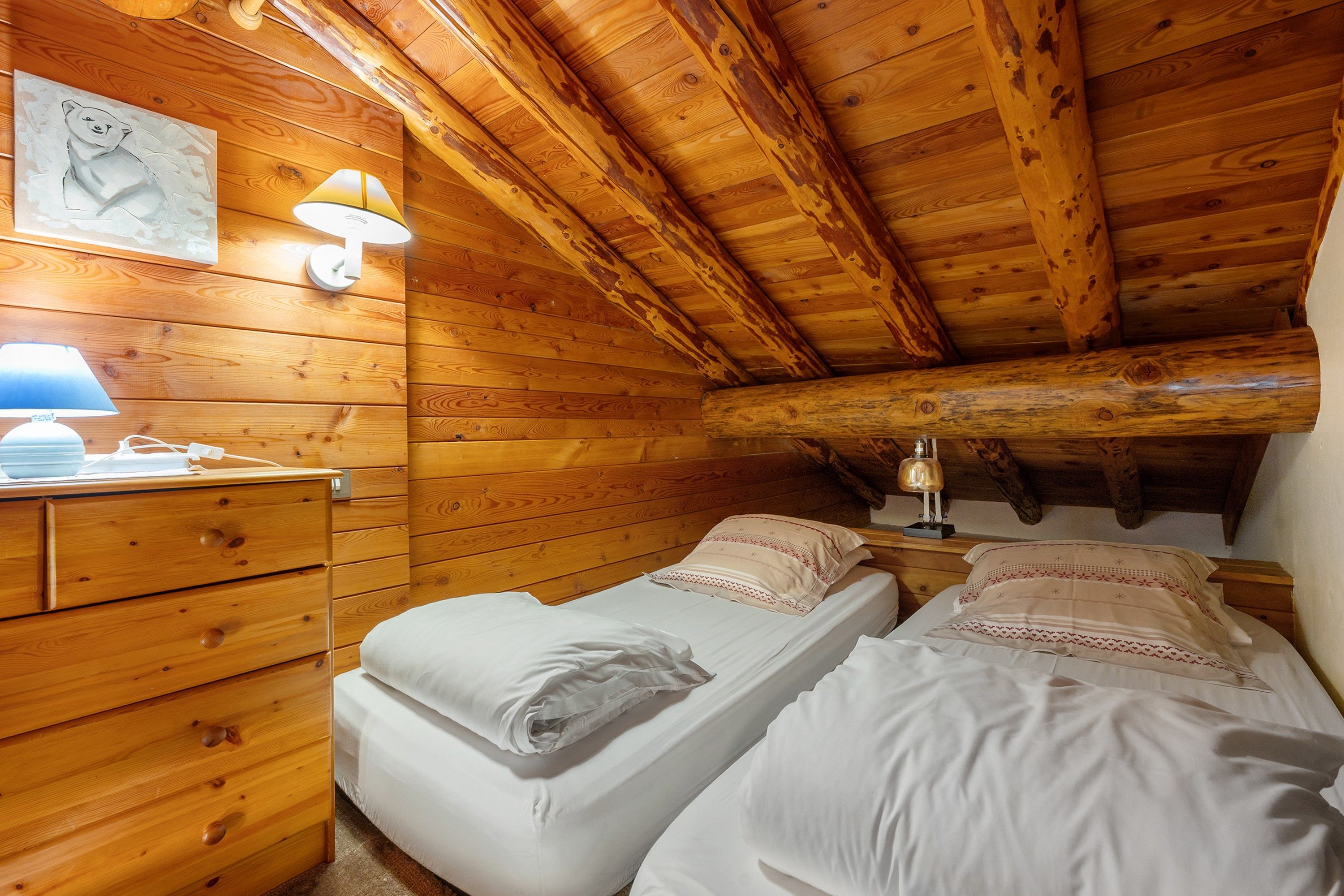 Een houten kamer met twee bedden, een nachtkastje, een lamp en een wandlamp.