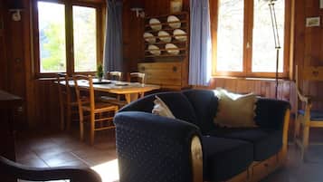 Interior de una cabaña de madera con comedor, sofá y una lámpara.
