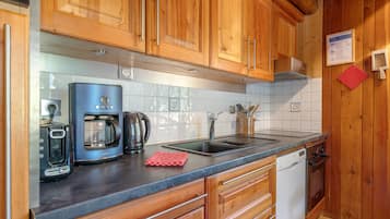 A kitchen with wooden cabinets, a coffee maker, a kettle, a sink, and a dishwasher.