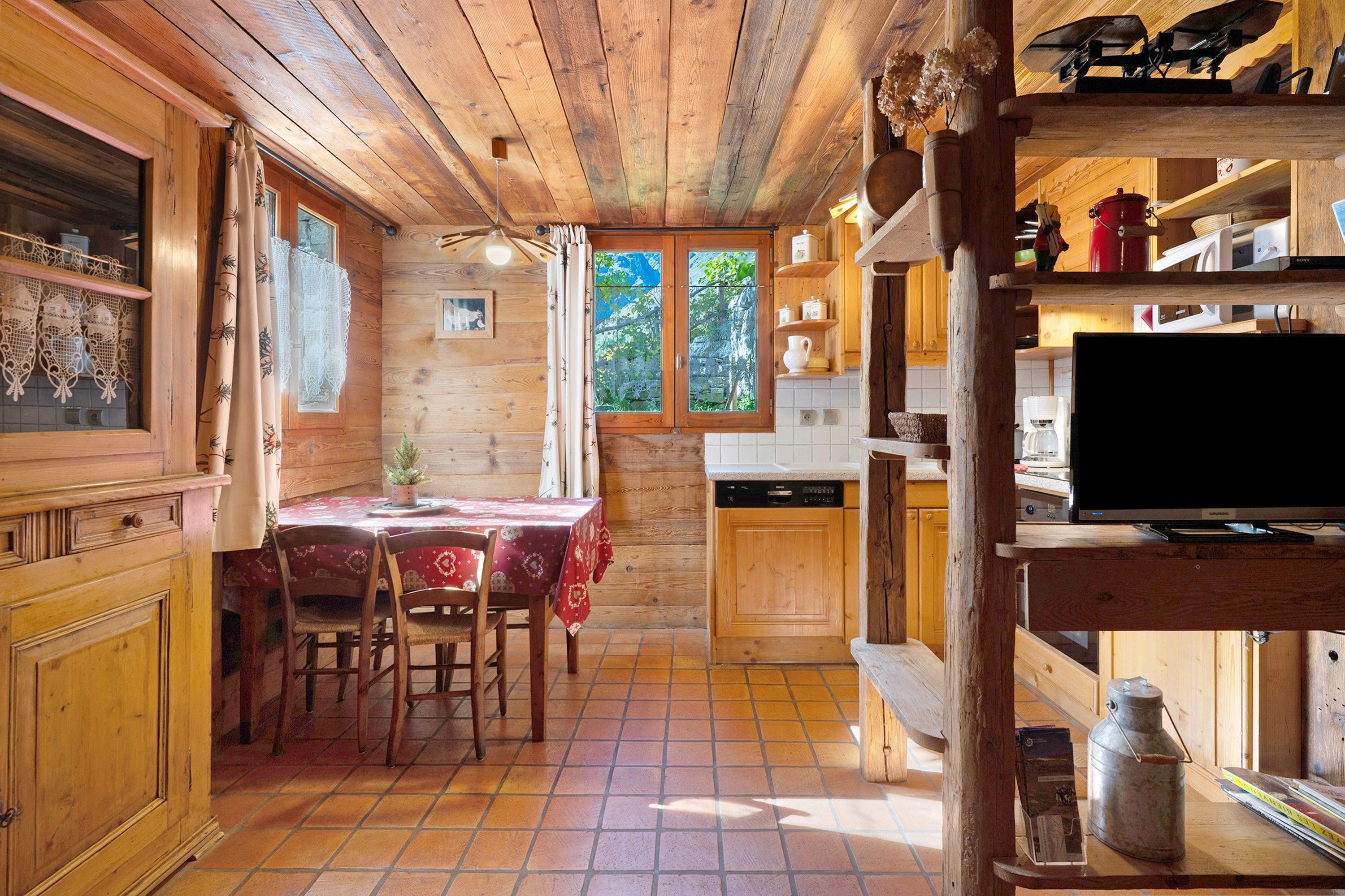 Een rustiek houten interieur met een eethoek, keuken en een televisie op een plank.