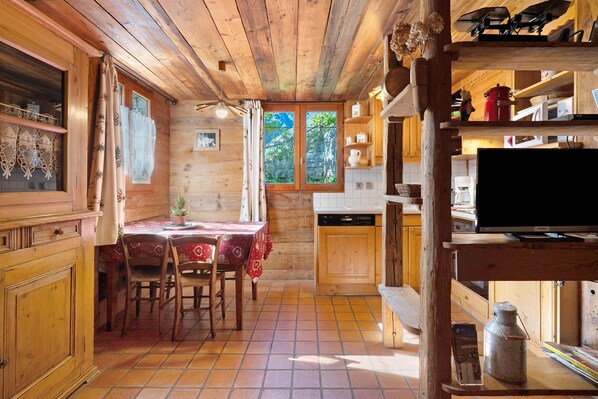 A rustic wooden interior with a dining area, kitchen, and a television on a shelf.