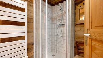 Eine Dusche mit Glastür, Holzvertäfelung und weiß gefliestem Boden.