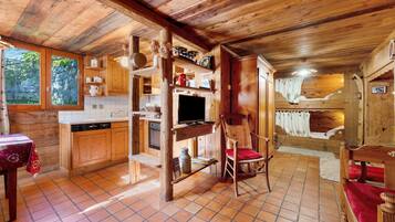 Ein rustikales Holzinterieur mit Küchenbereich, einem Esstisch mit rotem Tischlein und einem Holzstuhl mit roter Sitzauflage.