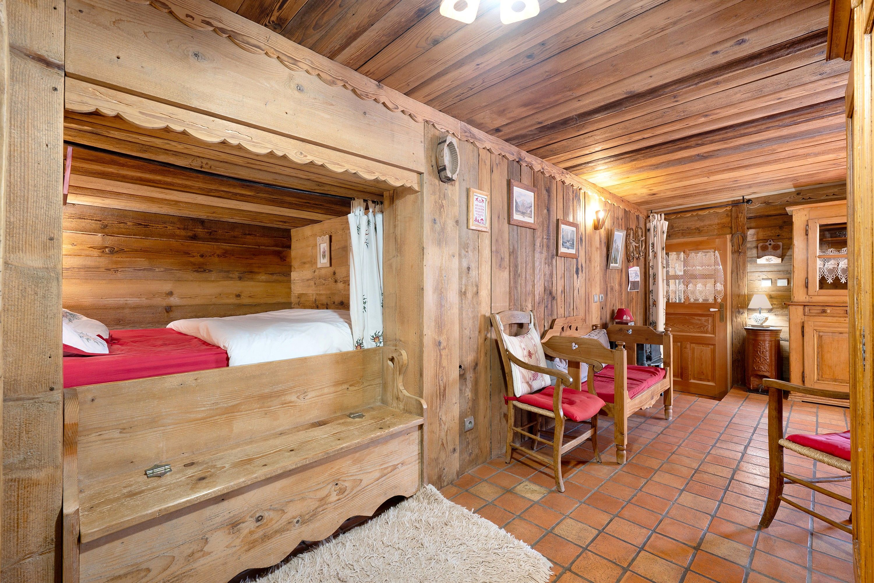 A wooden cabin interior with a bed, a chair, a table, and a cabinet.