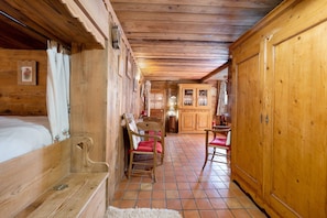 A wooden interior with a bed, chairs, a cabinet, and a tiled floor.