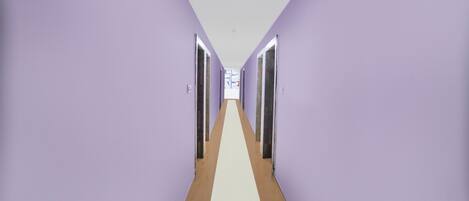 A long hallway with purple walls and a white floor, leading to a door at the end.