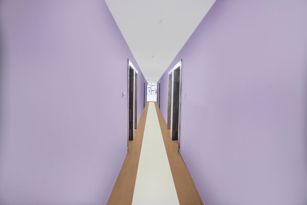 A long hallway with purple walls and a white floor, leading to a door at the end.