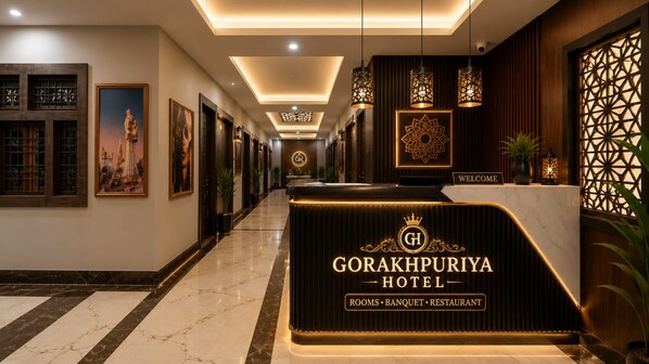 Zona de recepción de un hotel con piso de mármol, obras de arte enmarcadas y un mostrador de recepción con un logotipo.