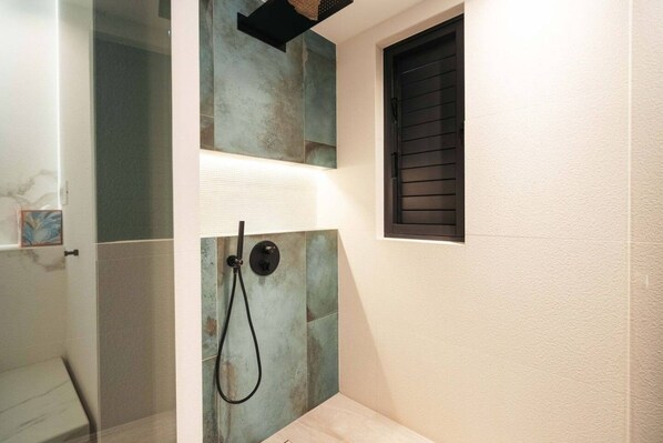 Eine Dusche mit Glastür, einem Handtuchhalter und einem Fenster mit Jalousien.