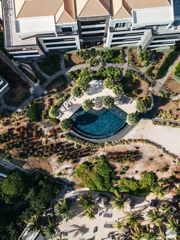 Ein Luftbild eines Resorts mit einem zentralen Pool, umgeben von Palmen und Liegebereichen.
