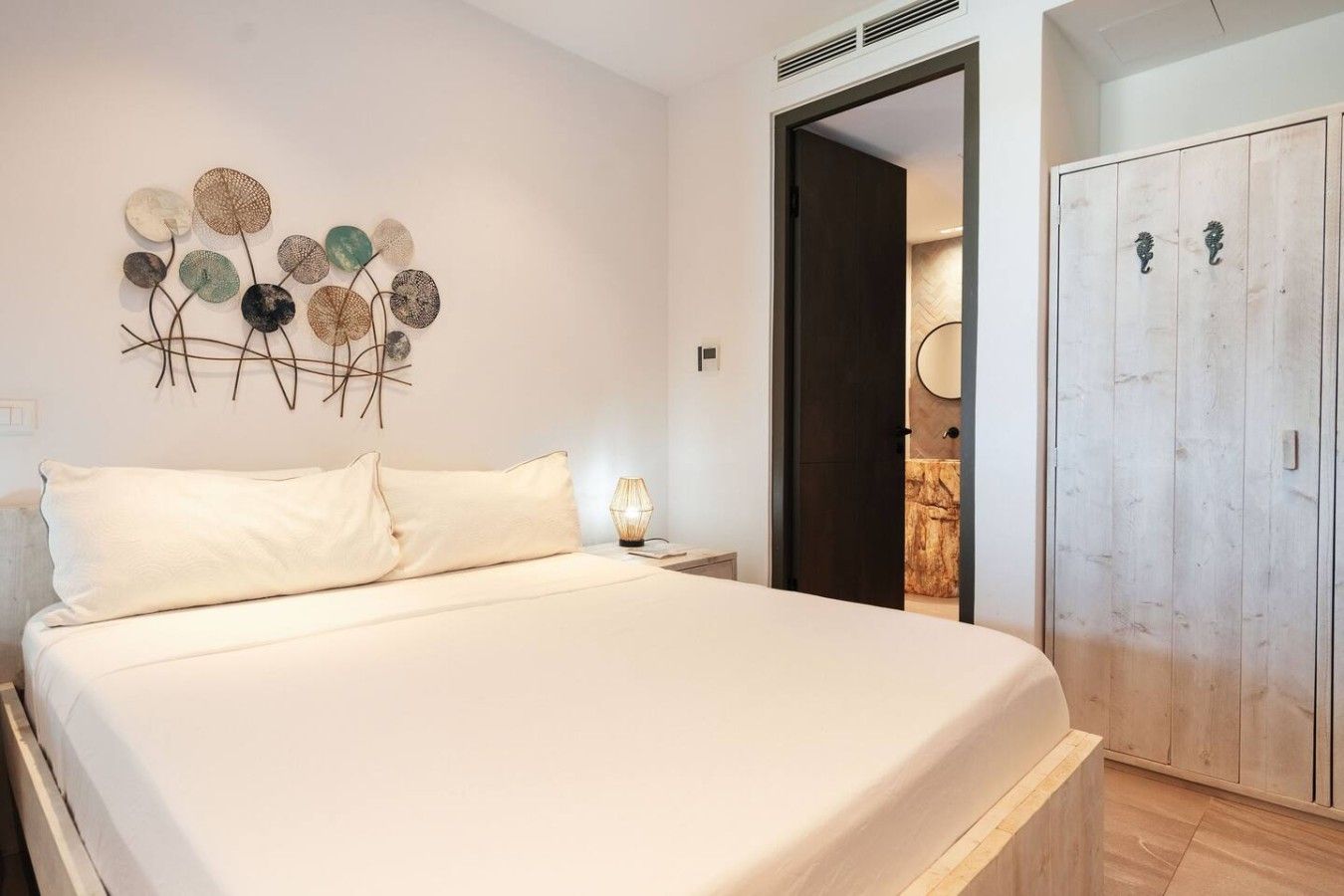 Un dormitorio con cama, una obra de arte en la pared, una mesita de noche, una lámpara y un armario.