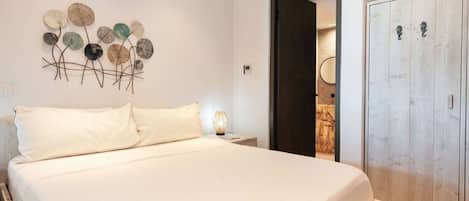 A bedroom with a bed, a wall art piece, a nightstand, a lamp, and a wardrobe.