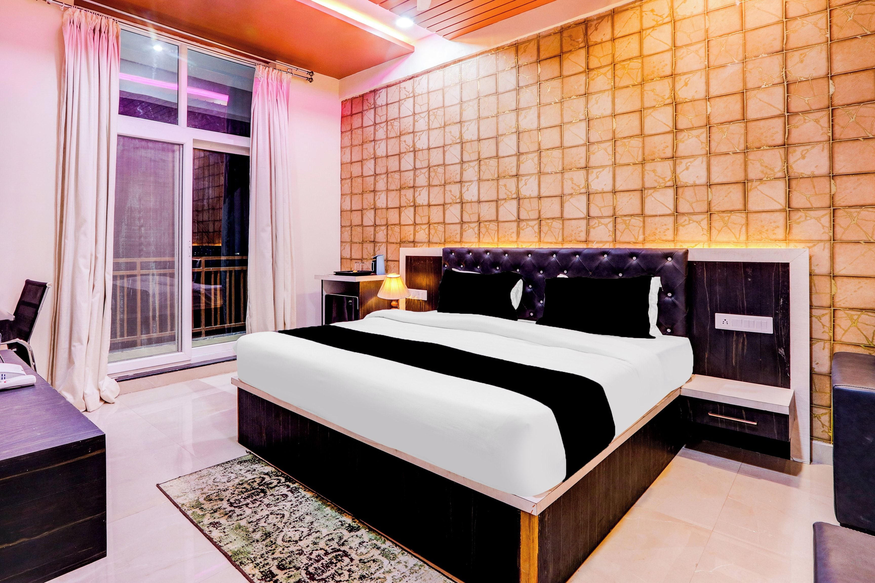 Une chambre d’hôtel moderne avec un grand lit, une table de chevet, un bureau et une vue sur l’extérieur, accessible par une porte coulissante.