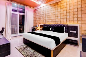 A modern hotel room with a large bed, a nightstand, a desk, and a view through a sliding door.