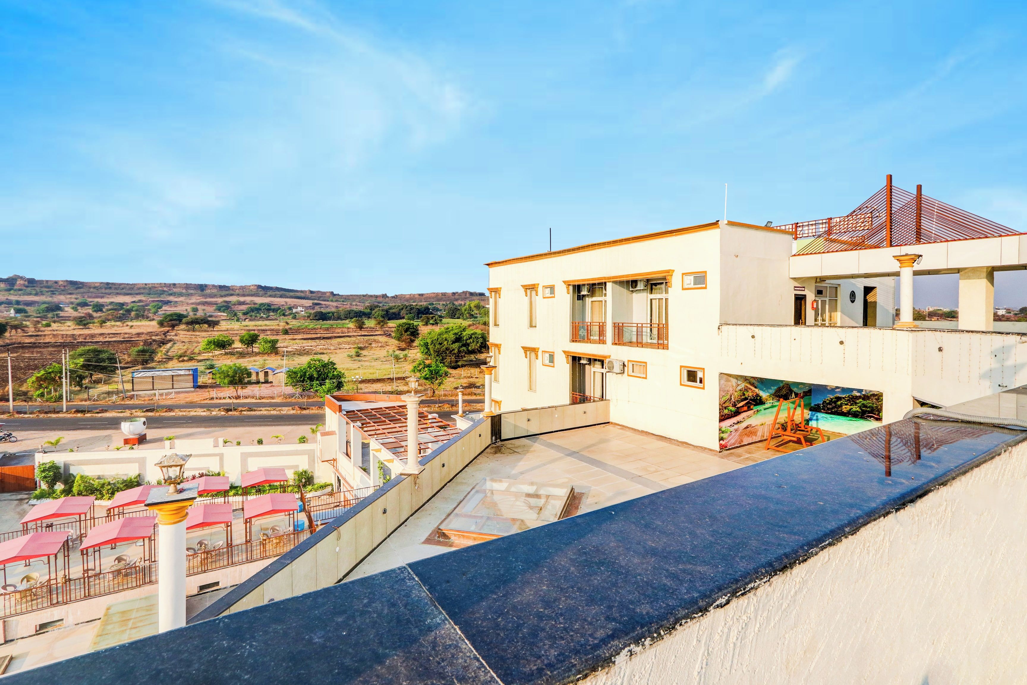 A modern building with a flat roof and a balcony overlooking a landscaped area with trees and a distant view of hills.