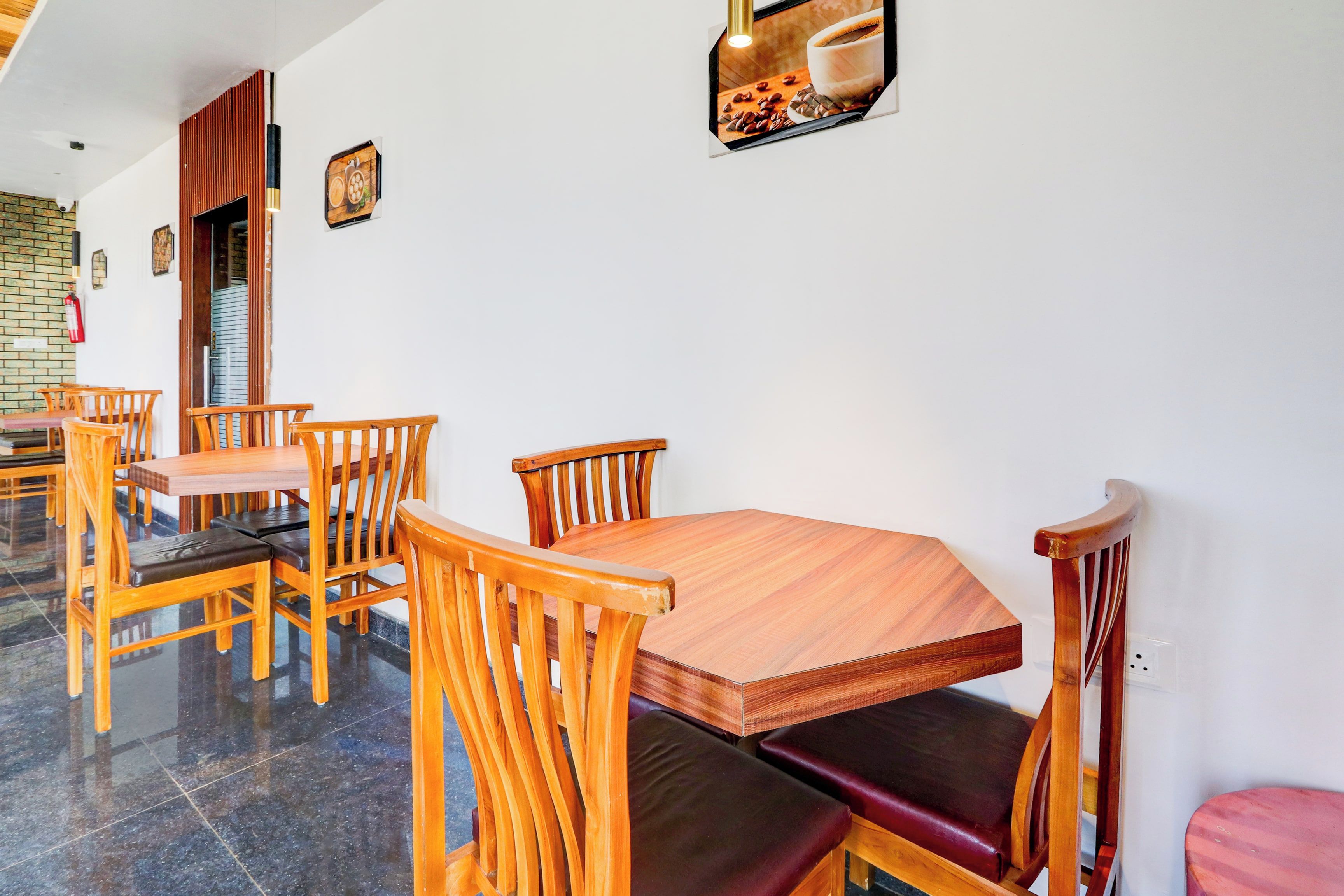A dining area with wooden tables and chairs, a fire extinguisher on the wall, and a framed picture above the table.