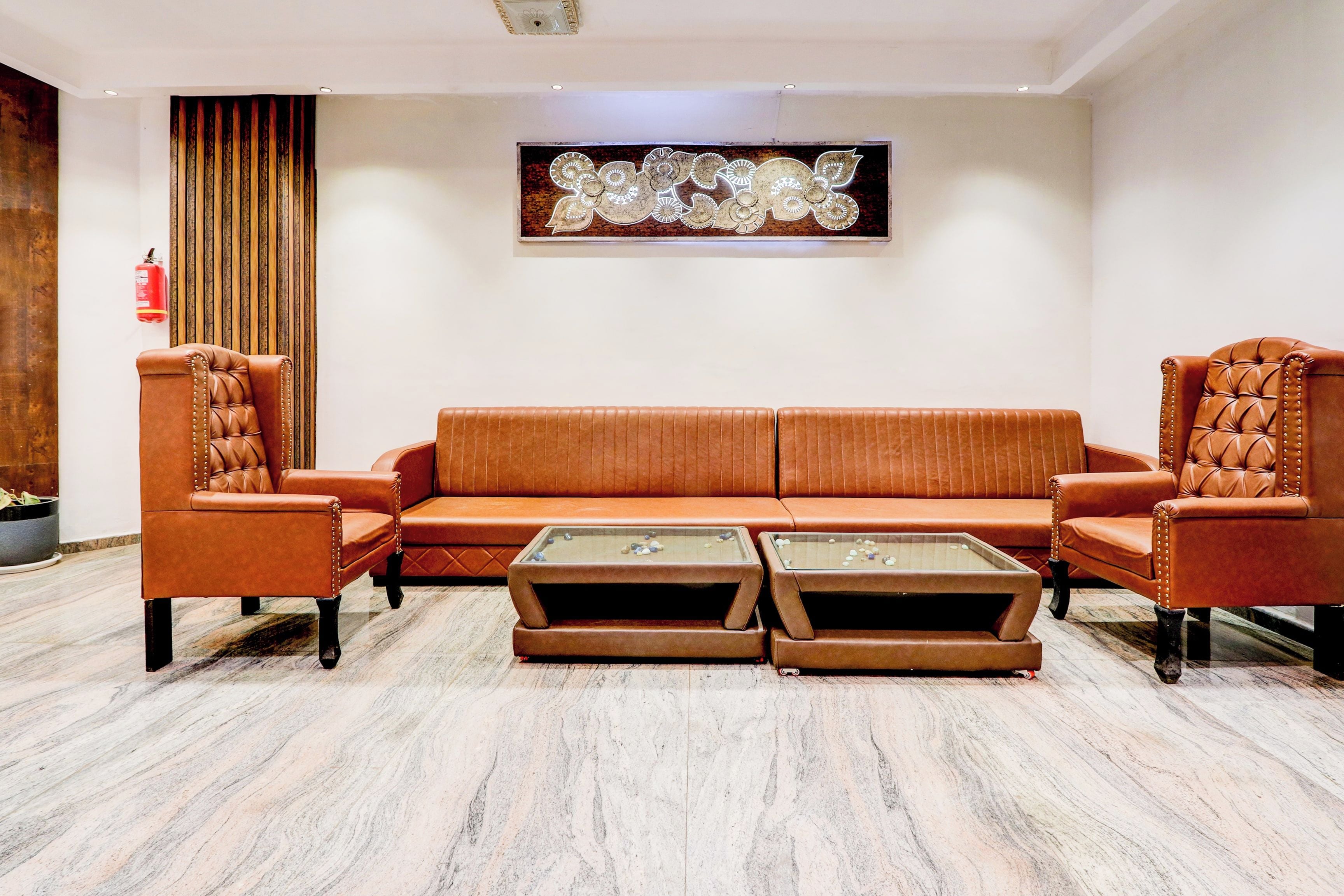 Una sala moderna con un sofá de cuero marrón, dos sillones y una mesa de centro de vidrio.