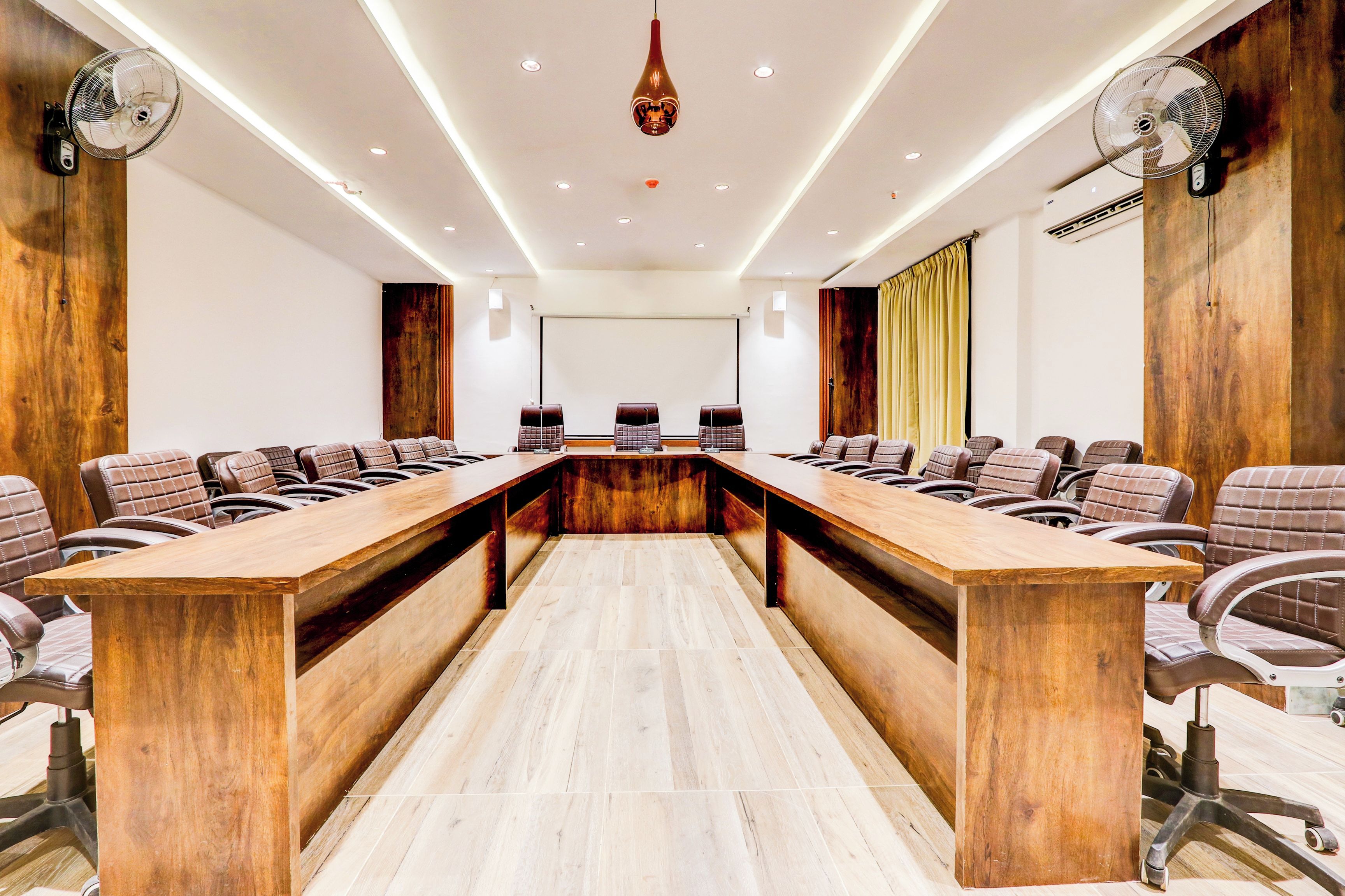 Un salón de conferencias con una larga mesa de madera, varias sillas y ventiladores de techo.