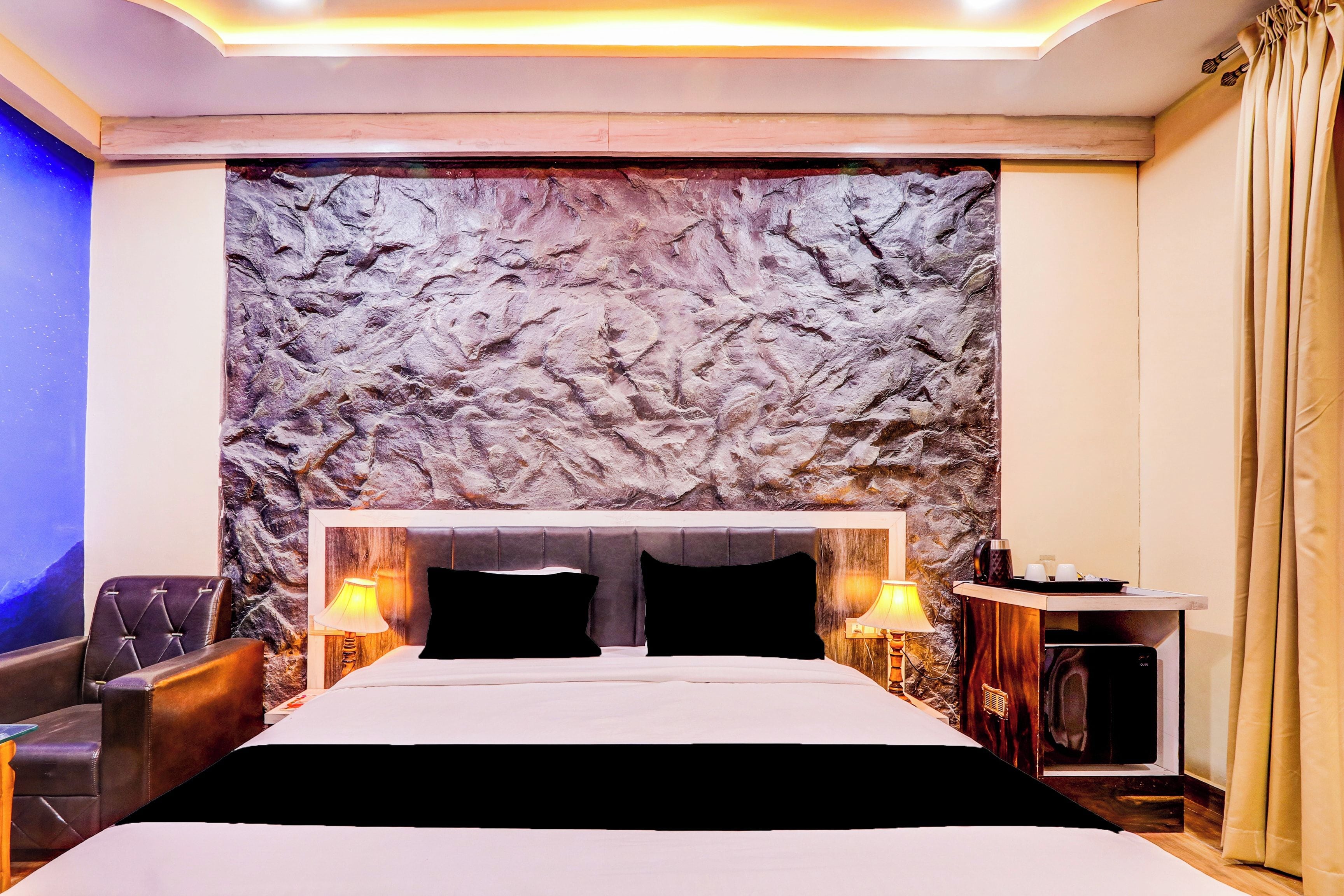Habitación de hotel con una cama grande, dos lámparas de noche, una mesita y una pared con textura decorativa.