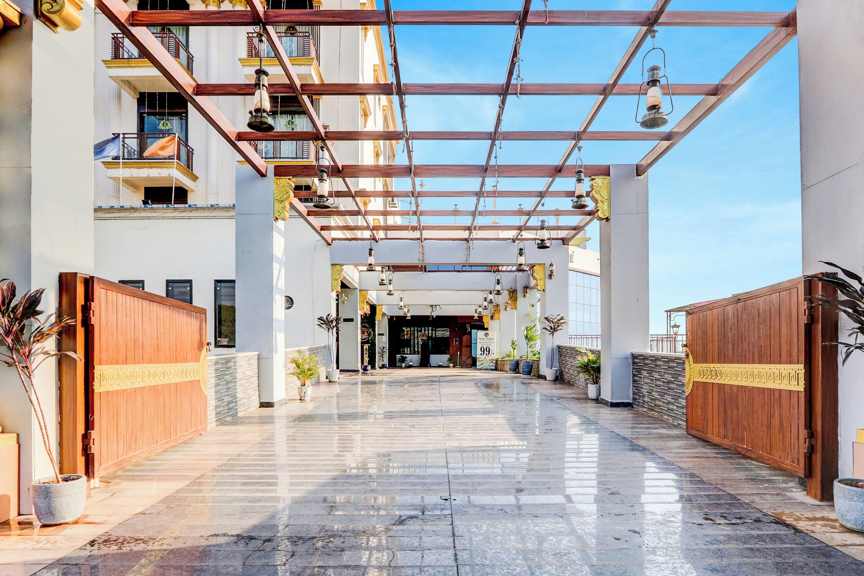 Entrada de hotel con un vestíbulo cubierto, plantas en macetas y cielo despejado.
