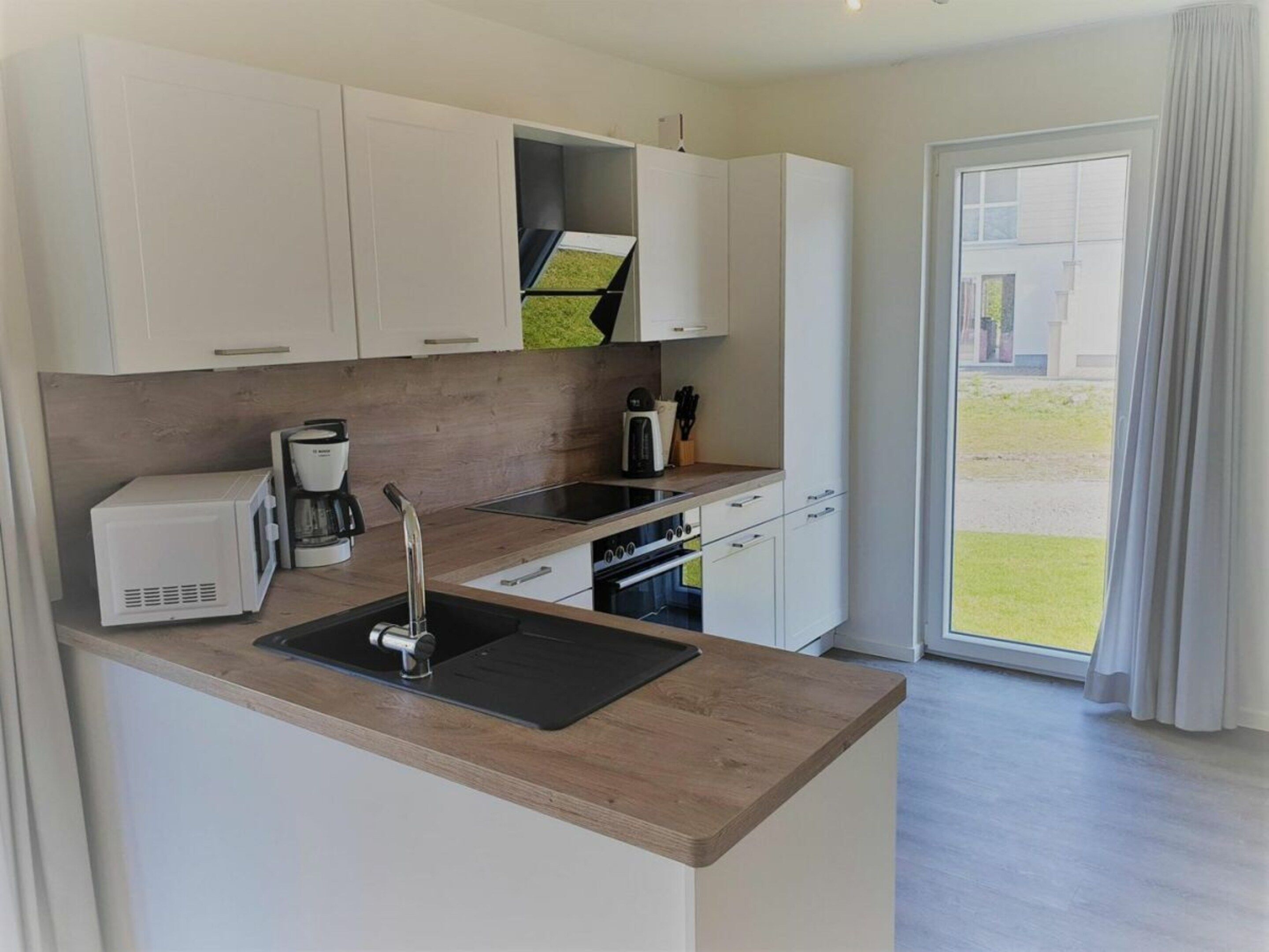 A modern kitchen with white cabinets, a wooden countertop, a built-in oven, and a coffee maker.