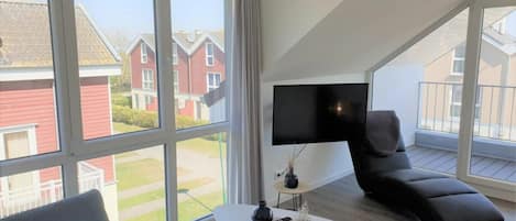 Una sala de estar moderna con un ventanal grande, un televisor de pantalla plana, un sofá y una mesita de centro.