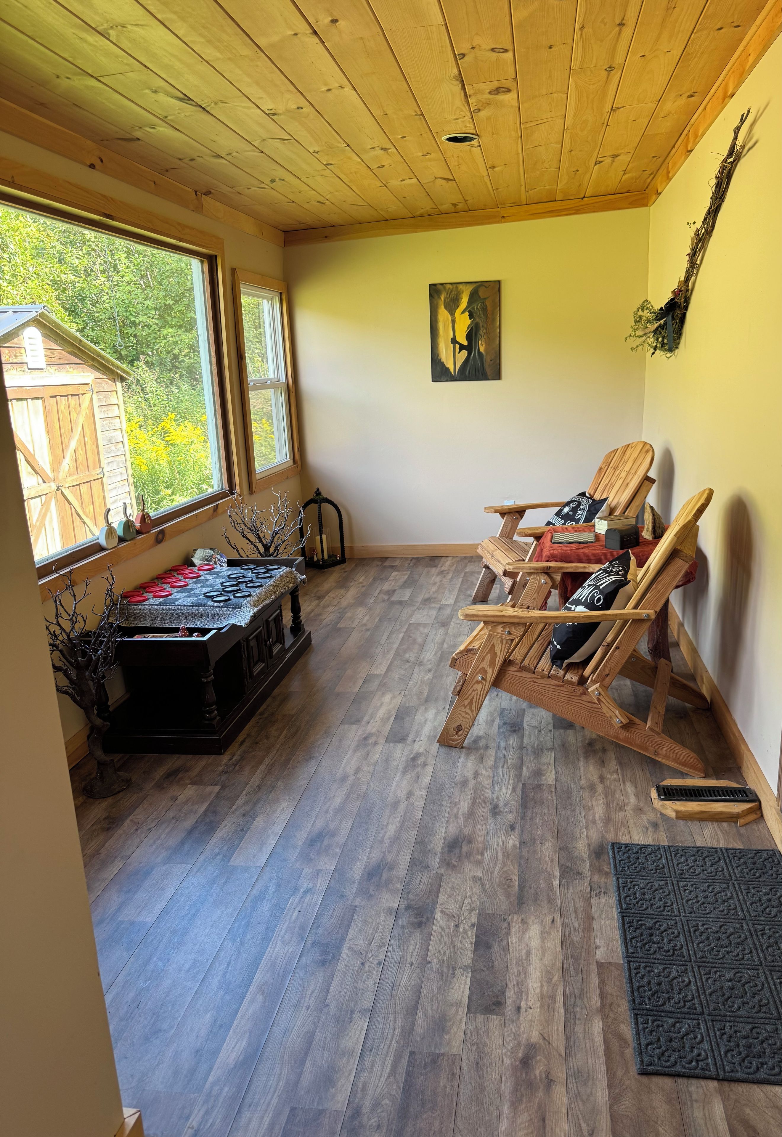 Een kamer met houten vloeren, een schilderij aan de muur en een raam met uitzicht op groen.