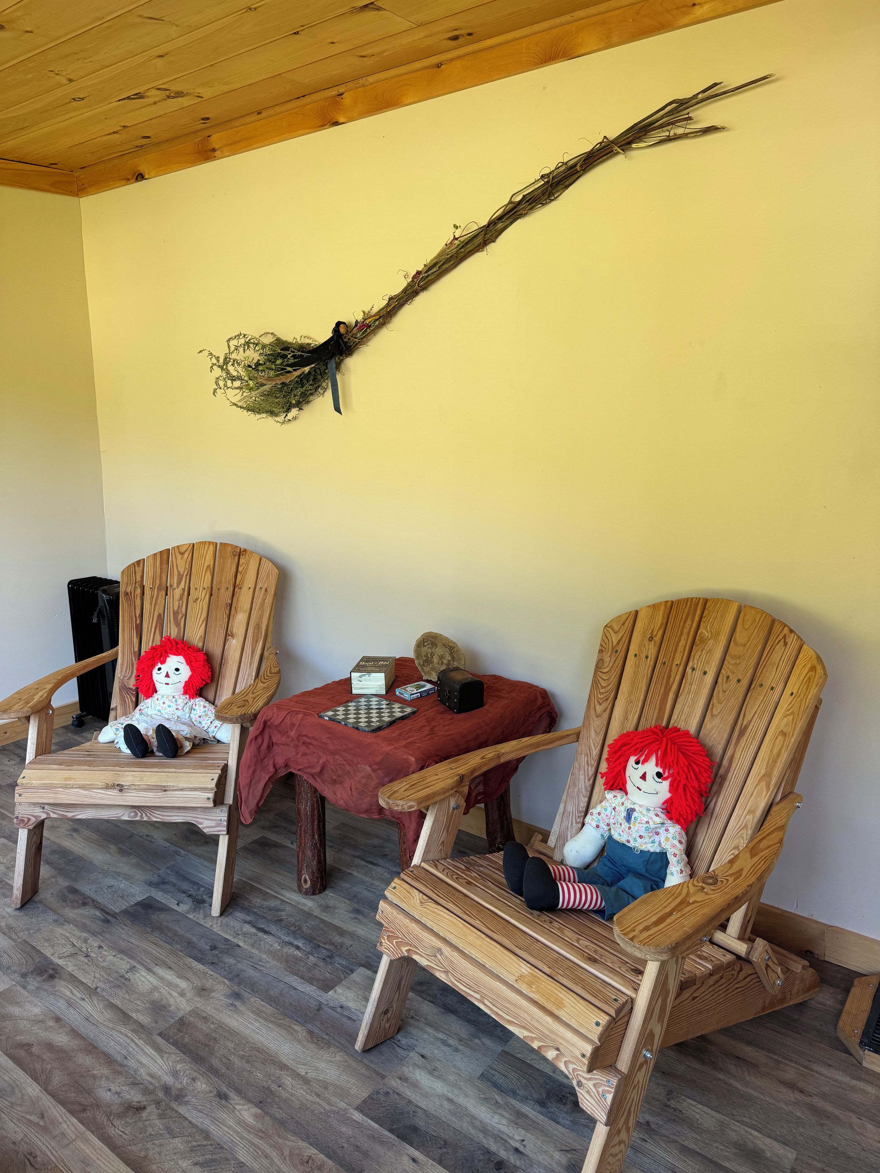 Two wooden chairs with plush toys, a chessboard, and a decorative branch on a wall.