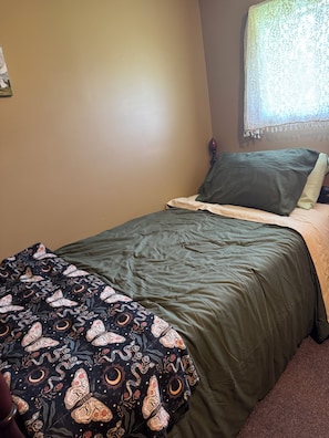 A bedroom with a bed, a window with lace curtains, and a wall with a floral pattern.