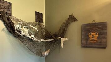 A room with a skeleton in a hammock, a wooden sign with a skull, and a wall-mounted picture.