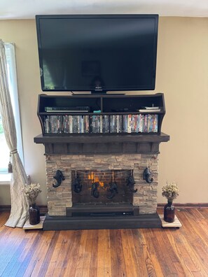 Un televisor de pantalla plana sobre una chimenea, con una colección de DVD y un fuste de piedra.