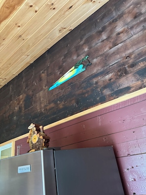 A rustic interior with a wooden ceiling, a decorative saw blade, and a vintage clock on a refrigerator.