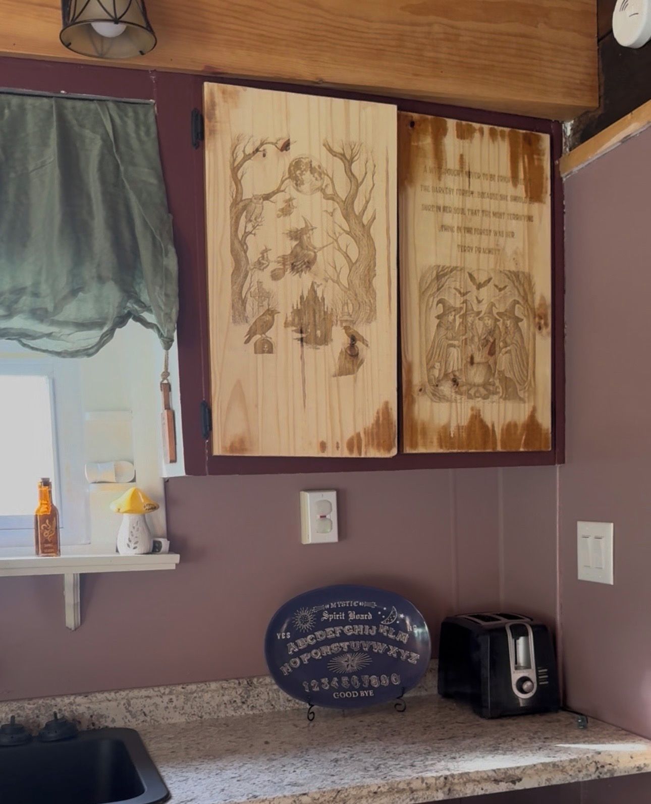 A kitchen with a wooden wall panel featuring a tree and bird illustrations, a blue coaster with a mystical theme, and a toaster on the counter.