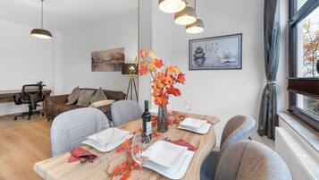 A dining area with a wooden table set for four, a vase with autumn leaves, and a painting on the wall.