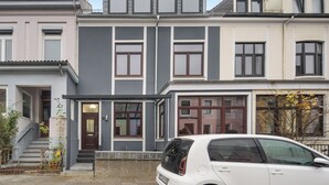 Una hilera de casas adosadas con entrada principal, escaleras y un coche aparcado.