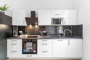 A modern kitchen with white cabinets, a built-in microwave, a coffee machine, and a kettle.