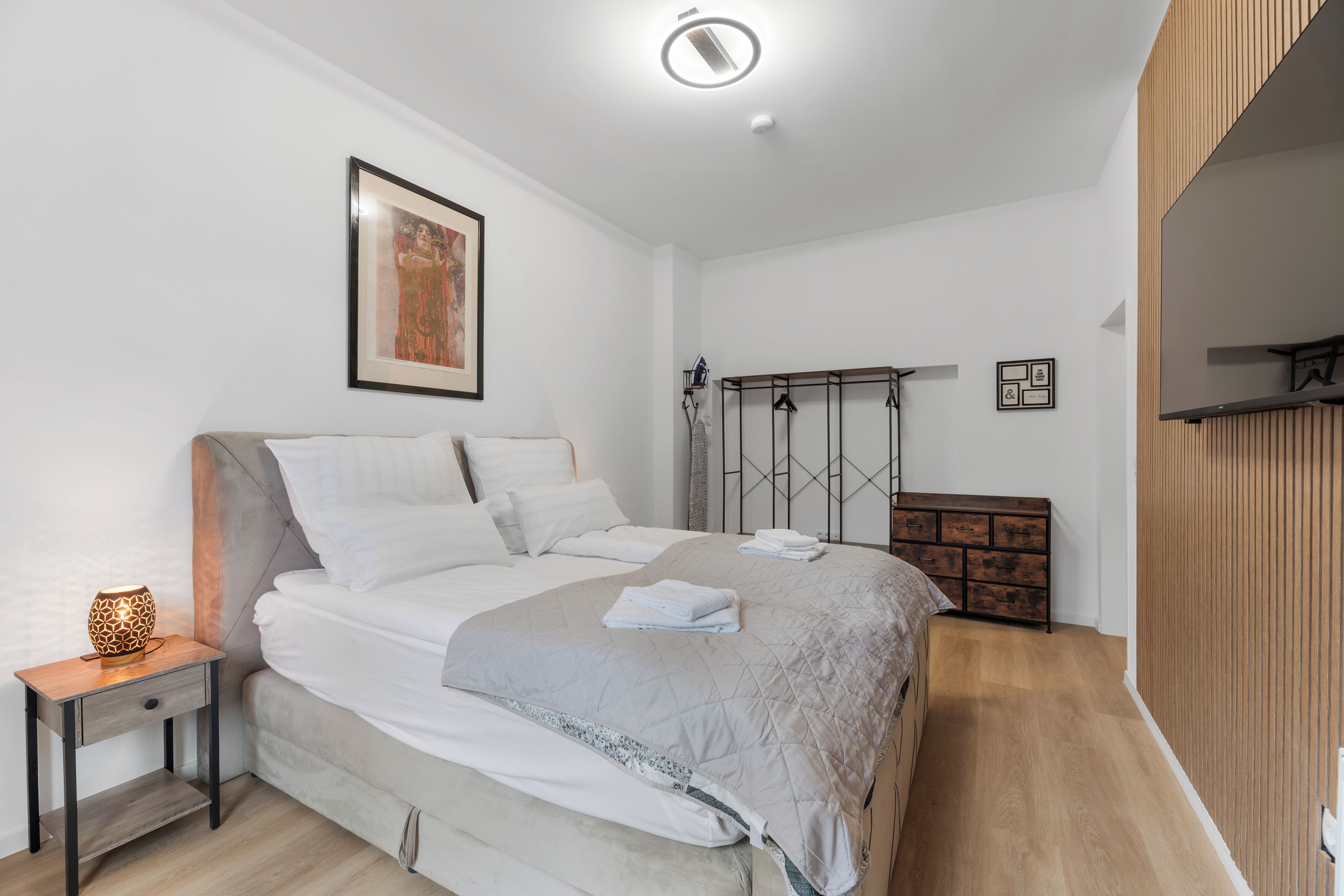 A modern bedroom with a bed, bedside table, and a wall-mounted shelf.